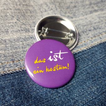 Ansteckbutton Das IST ein Kostüm / lila auf Jeans mit Rückseite