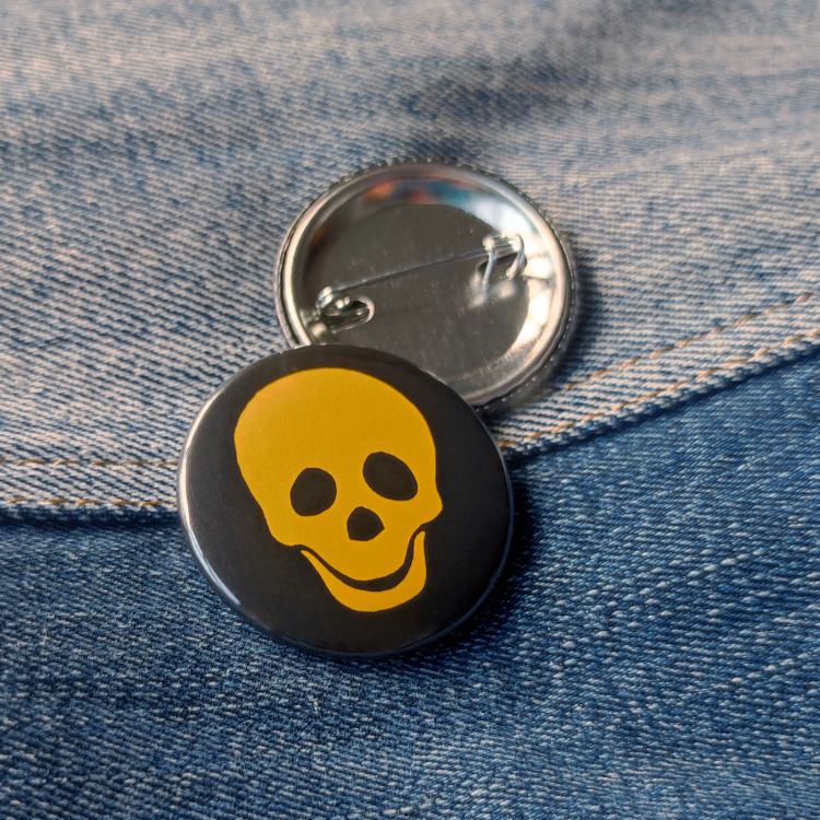 Ansteckbutton Totenkopf gelb auf Jeans mit Rückseite