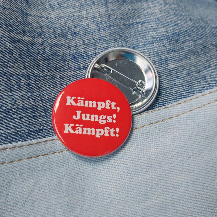 Ansteckbutton Kämpft, Jungs! Kämpft auf Jean mit Rückseite